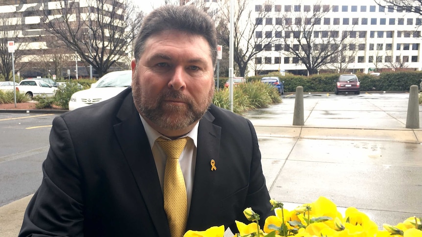 Peter Frazer is photographed next to yellow flowers as part of yellow ribbon week.