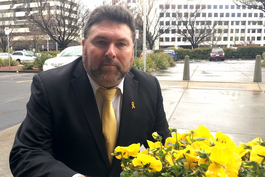 Peter Frazer is photographed next to yellow flowers as part of yellow ribbon week.