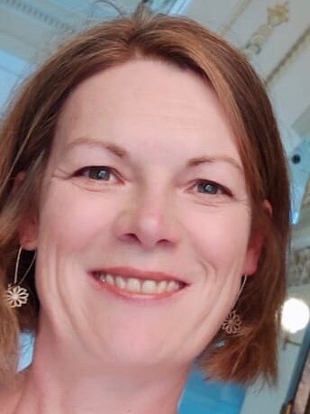 A closeup of a woman with shoulder length light brown hair wearing make up.