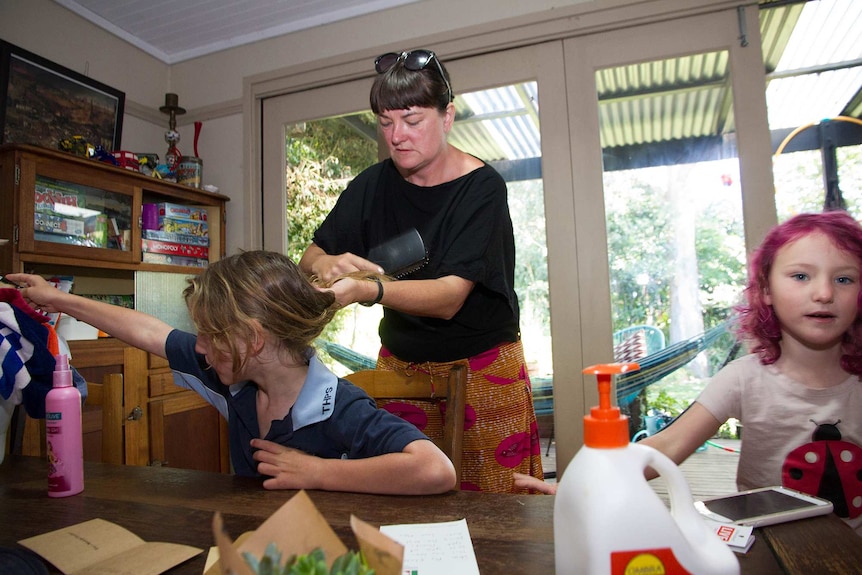 High school teacher Alison brushes her son's hair while her daughter looks on.