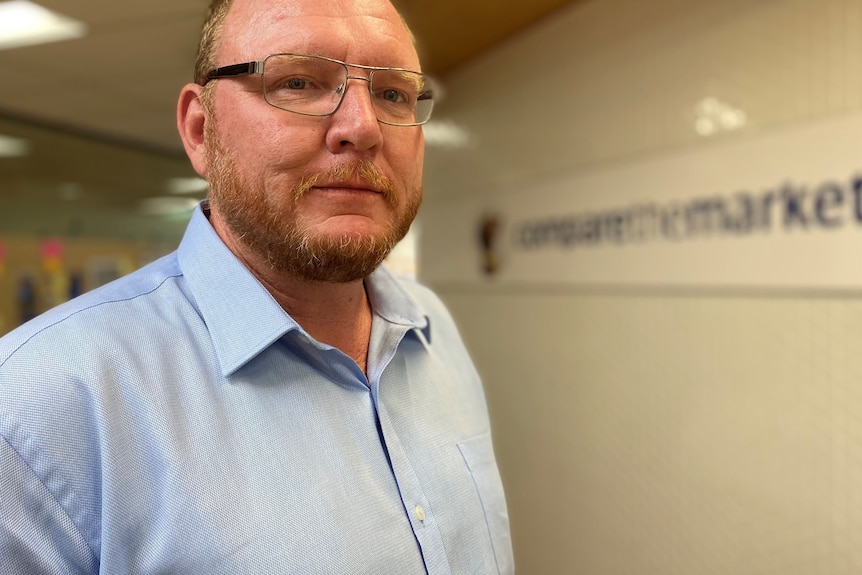 a man in a blue shirt in front of a company sign 