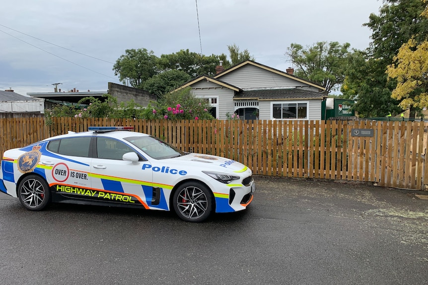 A police car parked in front of a house with a truck crashed into the back.