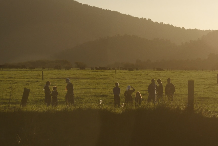 At sunset, children play on a farm, dressed in traditional outfits.