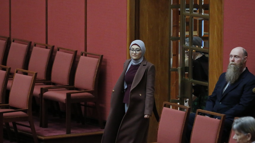 A woman in a hijab walks in the doors of the red Senate chamber.