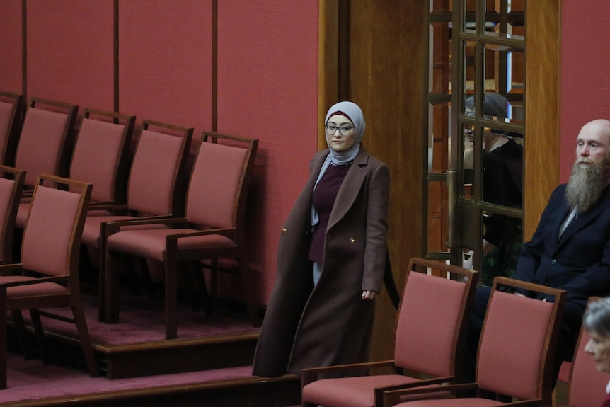 A woman in a hijab walks in the doors of the red Senate chamber.