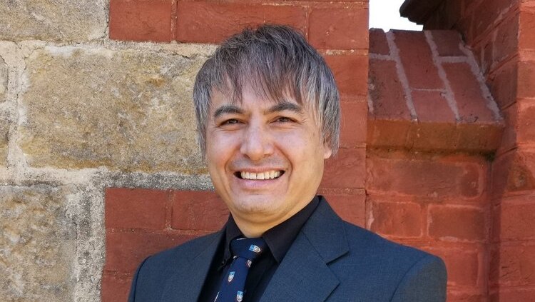 Professor Adrian Cheok wearing a suit standing in front of a brick wall