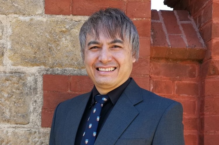 Professor Adrian Cheok wearing a suit standing in front of a brick wall