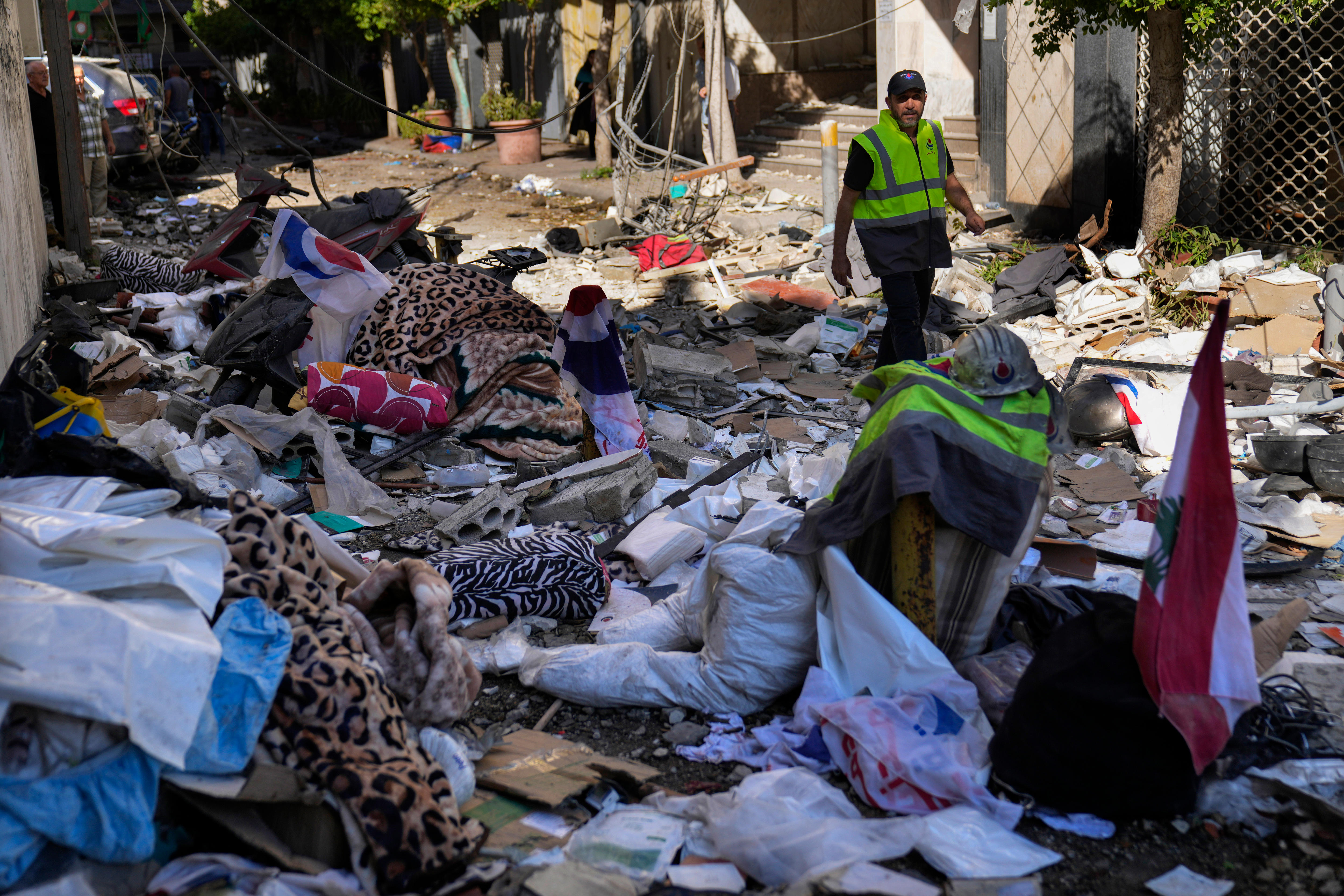 A man in a high vis vest walks through debris. 