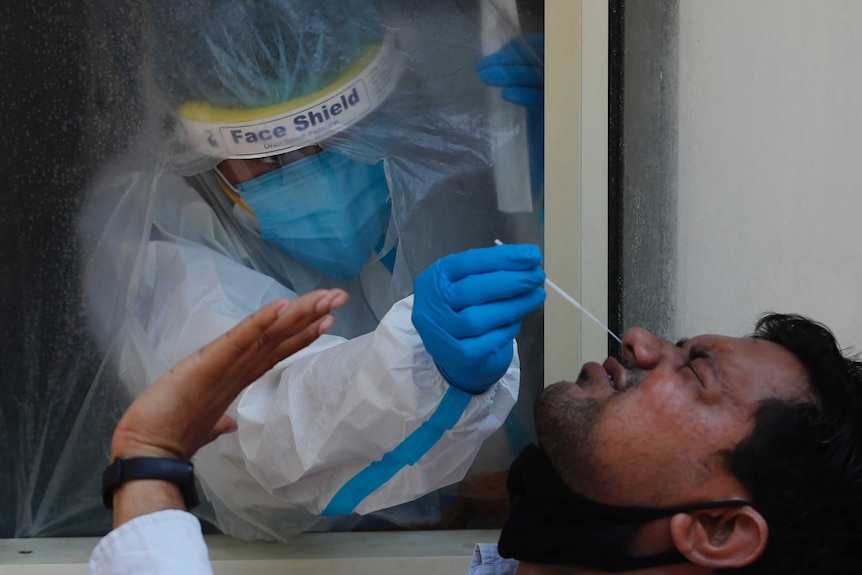 A man grimaces as a health worker in full PPE puts a swab up his nose.