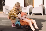 A small child pushing a younger child, who is sitting in a toy dump truck