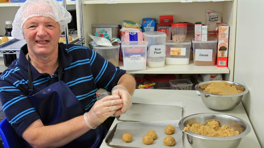 Man with a hairnet and gloves rolling biscuit mixture