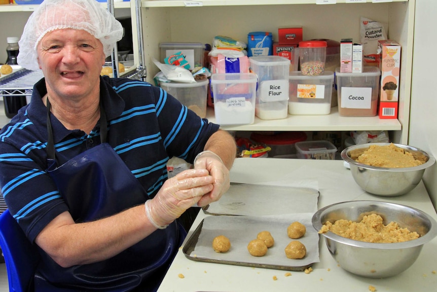 Man with a hairnet and gloves rolling biscuit mixture