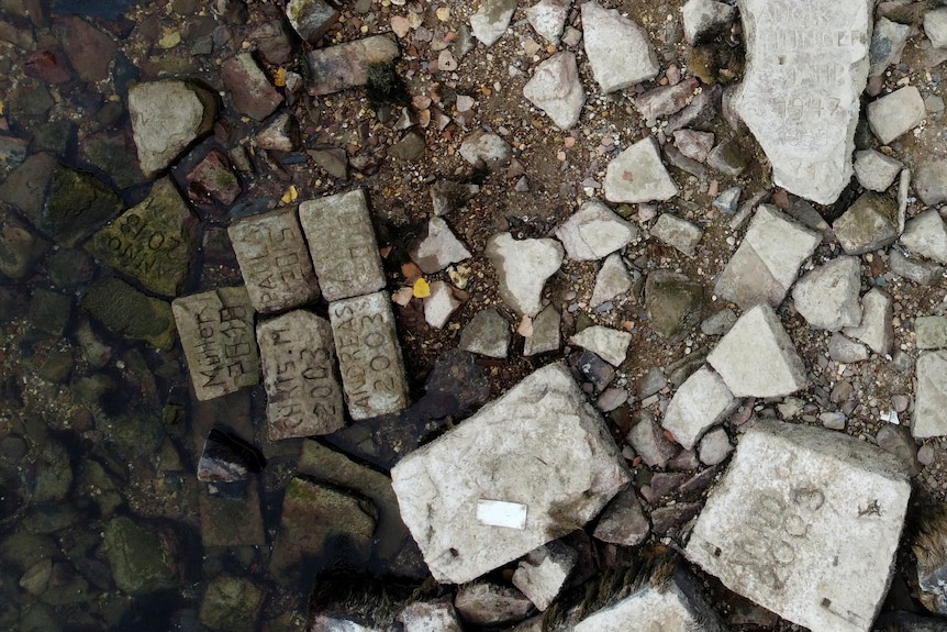 Veduta aerea di un fondale lacustre con diverse grosse pietre rettangolari.  Tutte le pietre hanno anni diversi scolpiti al loro interno