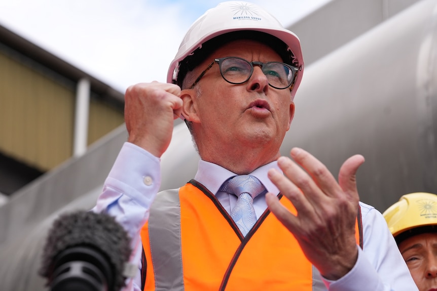Albanese wears a hard hat and high his vest as he speaks and gestures with his hands. 