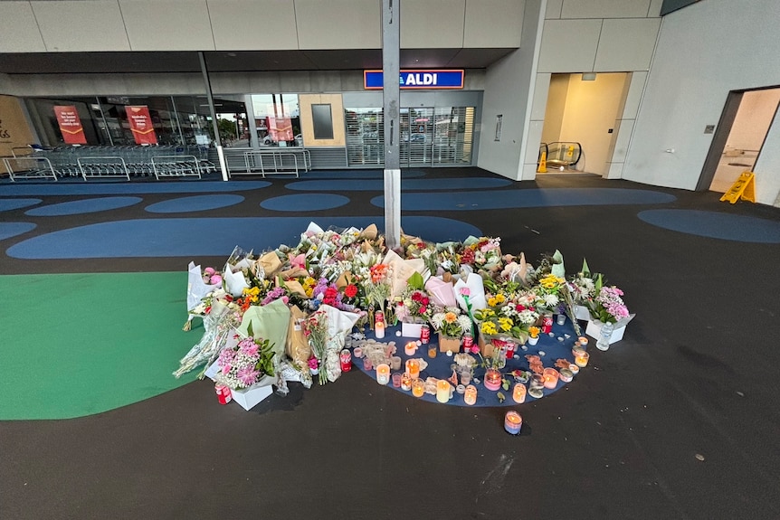 a pile of flowers and candles outside a shopping centre where a woman was murdered