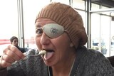 A woman wearing a beanie and an eye patch drinking a coffee
