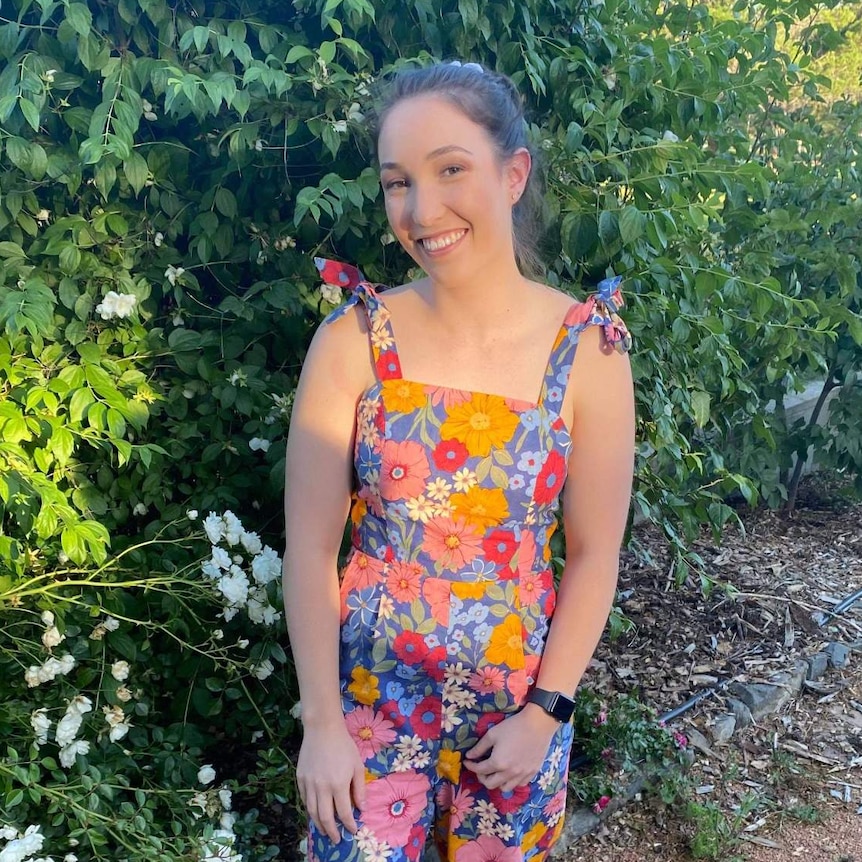 A young woman in a colourful dress smiles.