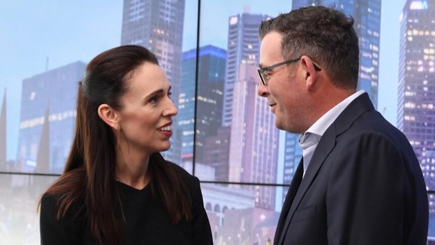 Jacinda Ardern and Daniel Andrews talking to each other in front of a sign of Melbourne city.