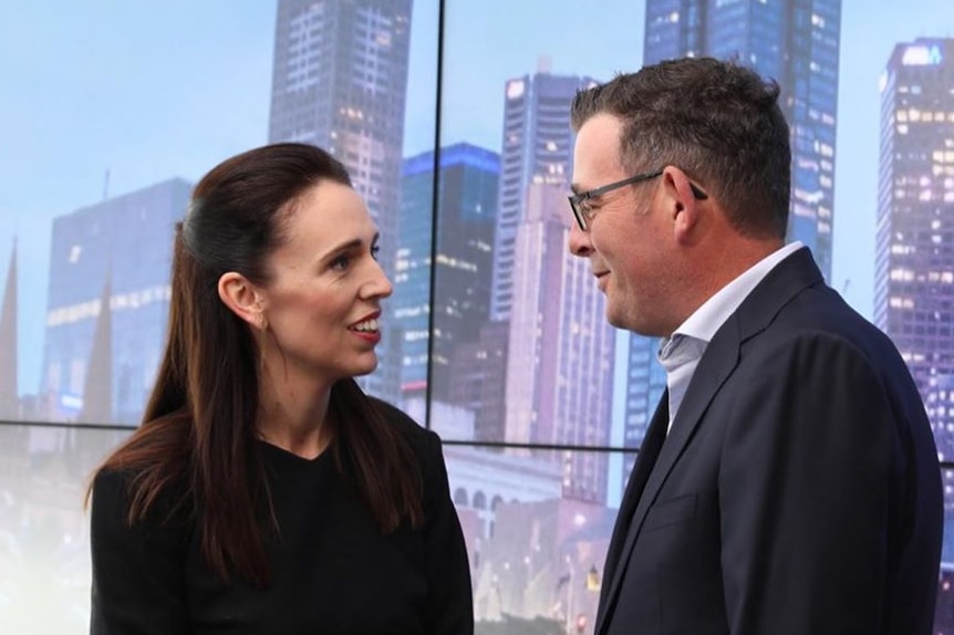 Jacinda Ardern and Daniel Andrews talking to each other in front of a sign of Melbourne city.