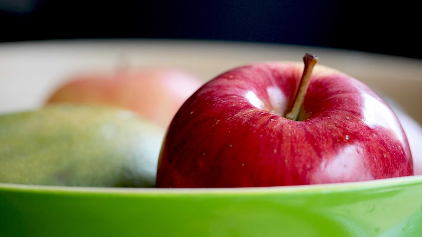 Red apple sits in green fruit bowl.