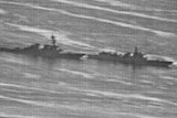 A grainy black-and-white photograph shows two warships approaching each other in open sea.