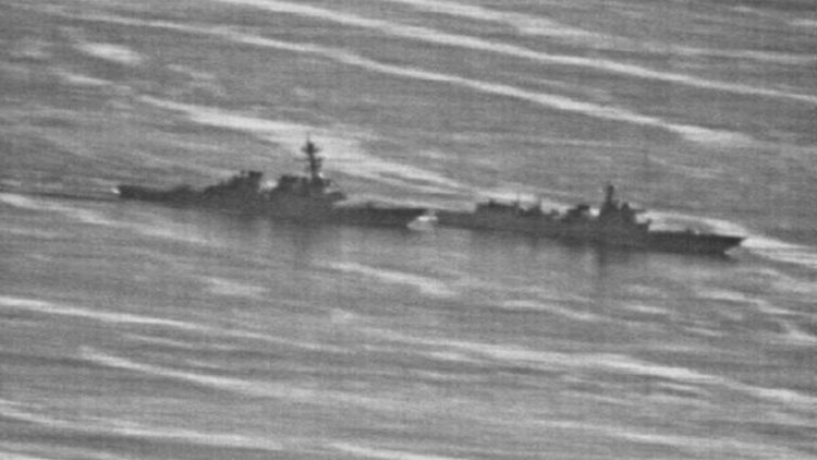 A grainy black-and-white photograph shows two warships approaching each other in open sea.