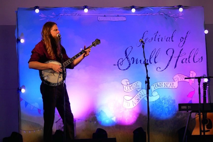A man plays a banjo on stage in front of a Festival of Small Halls banner