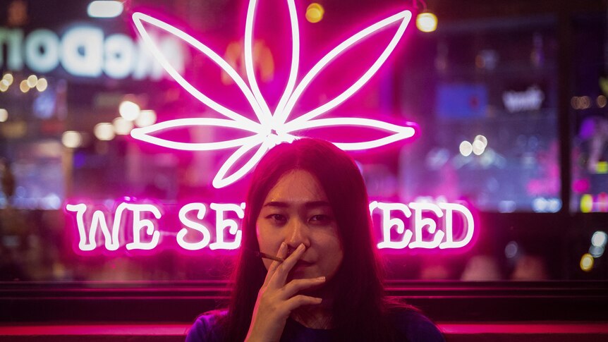 Woman smoking cannabis joint outside shop in Thailand.