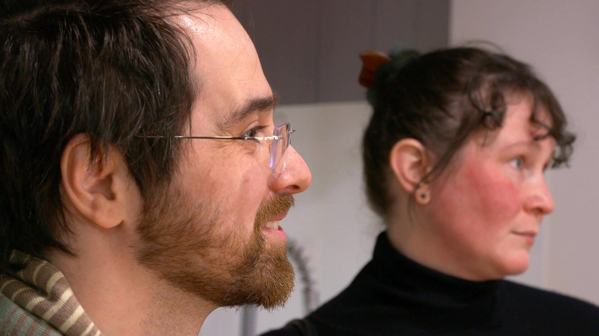 A man wearing glasses smiles next to a woman wearing a black top.