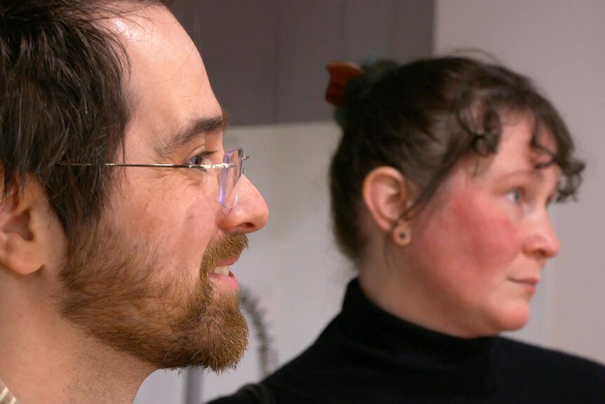 Un homme portant des lunettes sourit à côté d'une femme portant un haut noir.