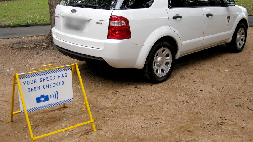 a warning sign about speed camera next to a car