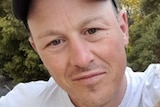 A selfie-style shot of a dark-eyed man wearing a cap.