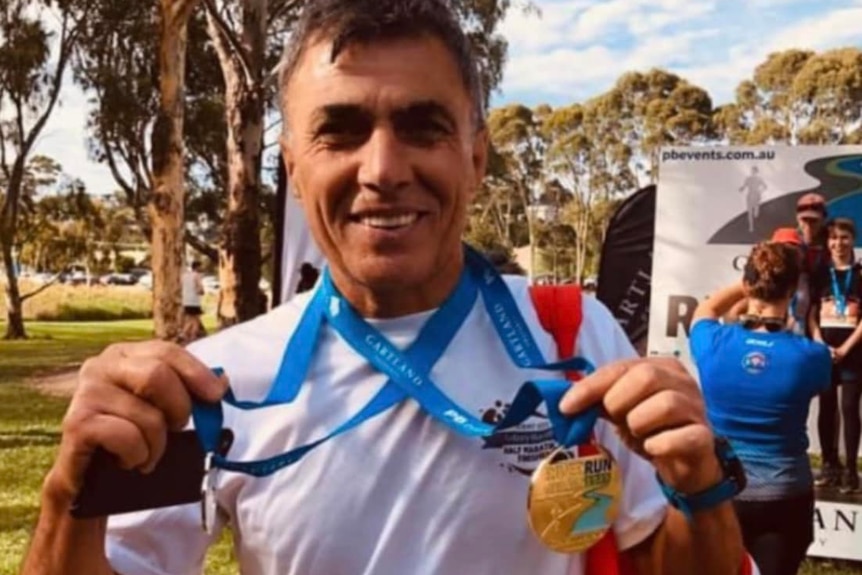 Suat Bayram smiles holding medals from a marathon