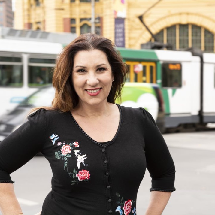 A smiling woman stands in front of Flinders Street Station, while a tram passes by.