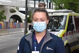 A woman wearing nursing scrubs and a face mask.