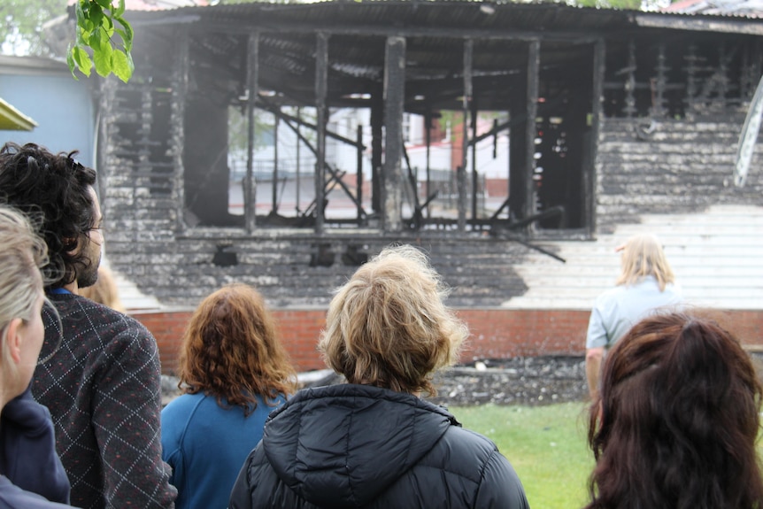 The back of six people standing in front of a fire damaged building