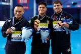 Three male divers pose for a photograph holding their medals at the 2024 World Aquatics Championships.