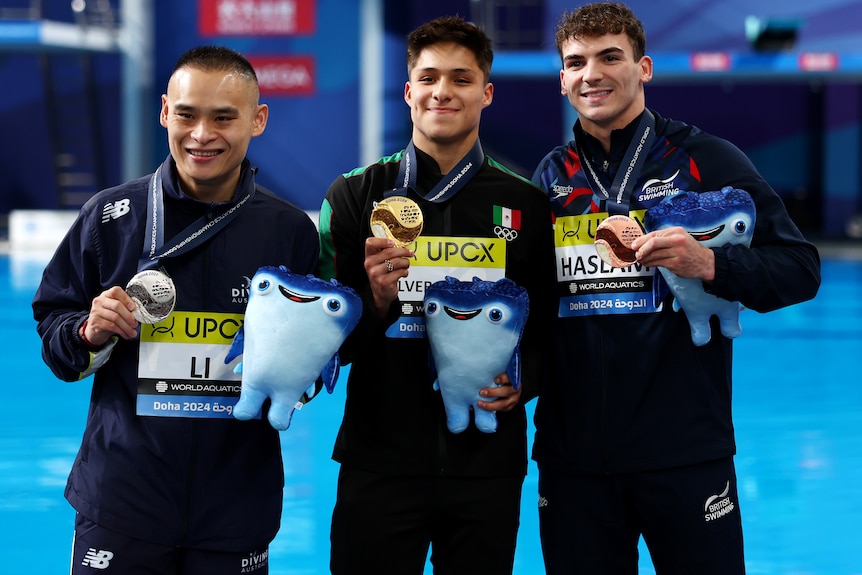 Three male divers pose for a photograph holding their medals at the 2024 World Aquatics Championships.