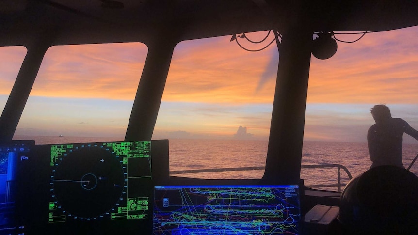 The orange hues and clouds on the horizon as viewed through the window of a trawler wheelhouse