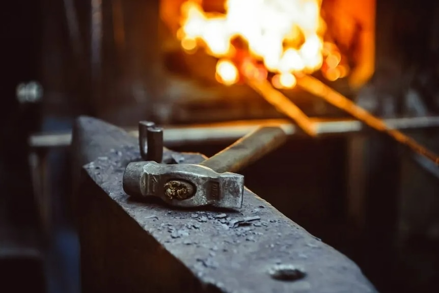 A hammer sitting on an anvil with a hot forge in the background.