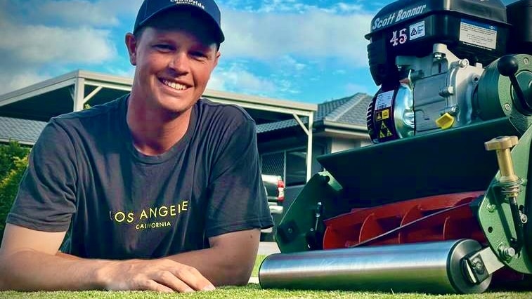 Alex Quinn laying on his lawn beside his mower.