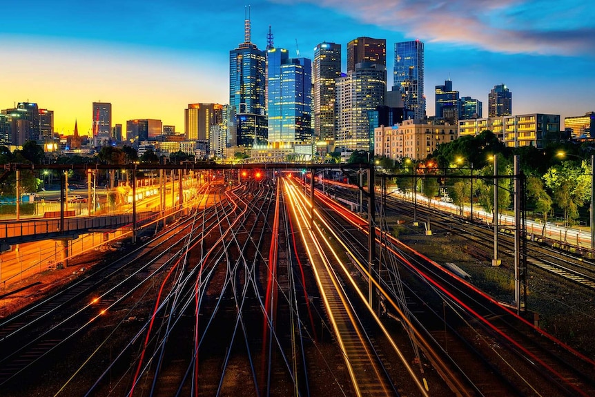 Train lines illuminated at sunset in front of the City of Melbourne skyline.