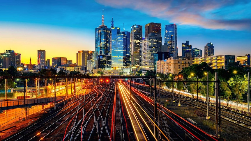 Train lines illuminated at sunset in front of the City of Melbourne skyline.