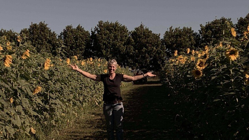 Michele Stephens stands between rows of sunflowers on her vegetable farm.