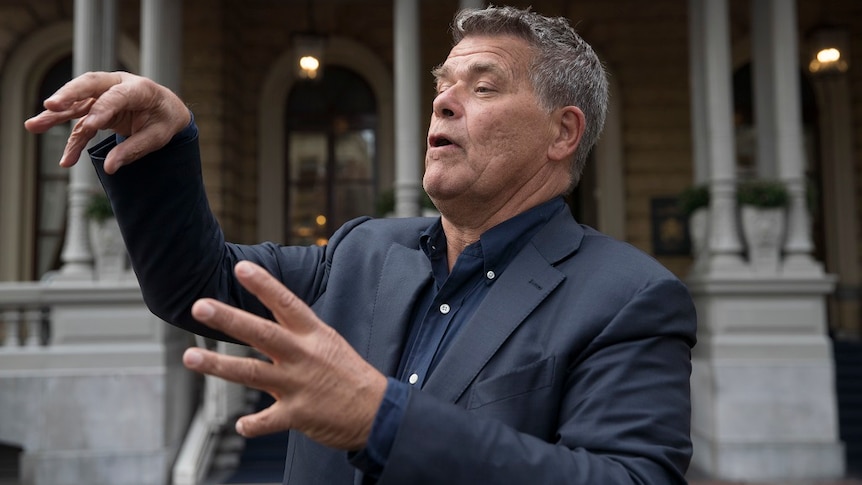 A man gestures with his hands while speaking to reporters outside a courthouse.