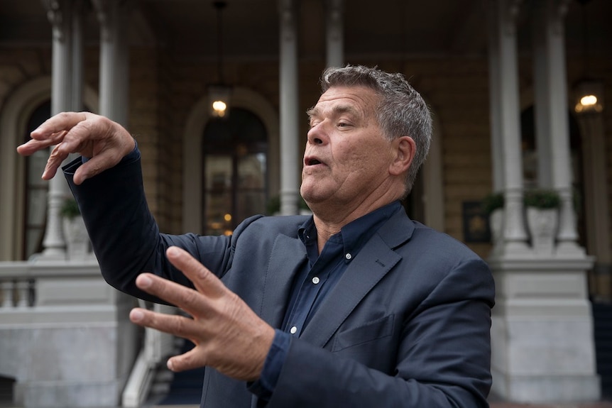 A man gestures with his hands while speaking to reporters outside a courthouse.