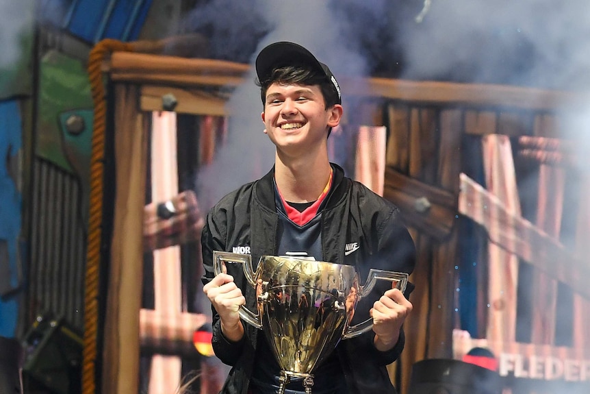 A teenager in a cap on a stage smiling and holding trophy.