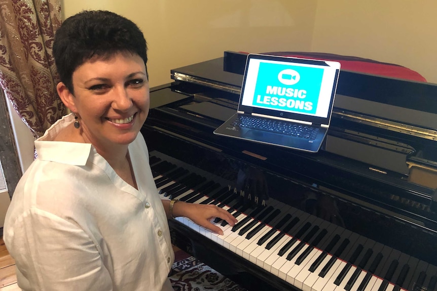 Karyn Skewes sits at a grand piano with a laptop in front of her