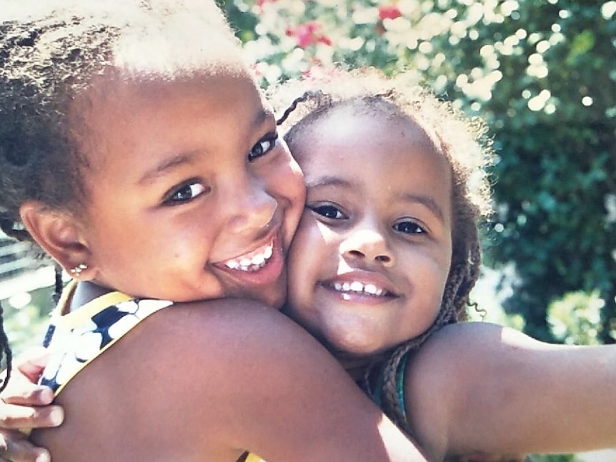 Two smiling children hug each other.
