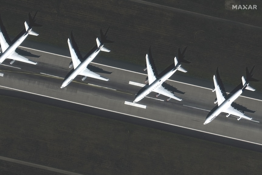 A satellite image shows four passenger planes parked and idle on a runway